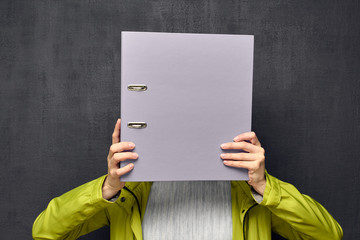 Portrait of girl hiding face behind big folder