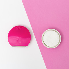 Womens beauty and hygiene products, red elecrtic face brush and cotton pads on white and pink paper background. Facial treatment. Flat lay style. Top view.