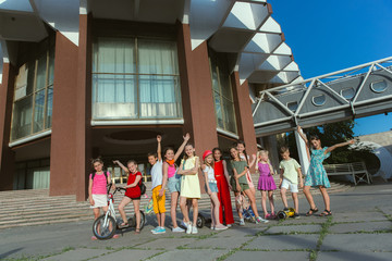 Happy kids playing at city's street in sunny summer's day in front of modern building. Group of happy childrens or teenagers having fun together. Concept of friendship, childhood, summer, holidays.