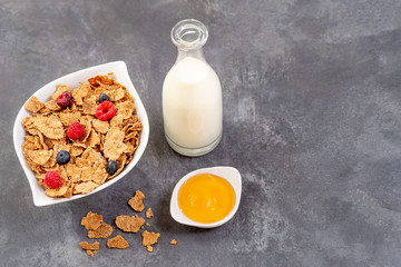 Healthy breakfast with bowl of cereal, honey, and fruits on grey slate background.