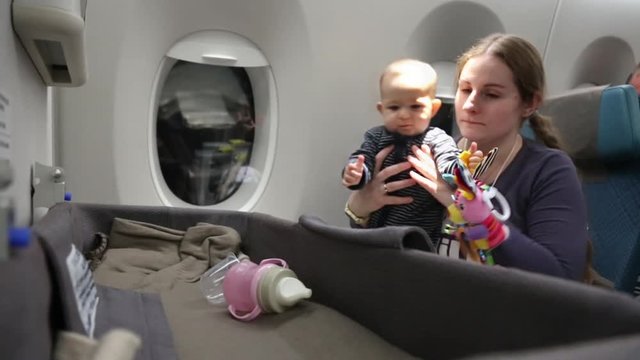 Mother with a happy small child on the plane, a woman holds a baby who takes a toy from a special bassinet