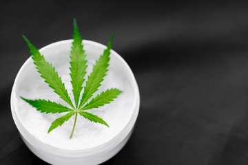 Top view of a jar with CBD or hemp salve with cannabis leaf on black background. Marijuana cream. Cannabidiol topicals concept with copy space