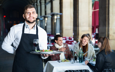 Obraz premium Portrait of smiling waiter with serving tray meeting restaurant guests