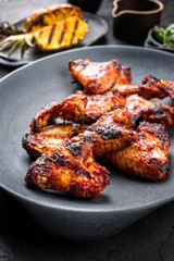 Exotically barbecue chicken wings with hot chili sauce, jalapeno and pineapple as closeup on a cast iron plate