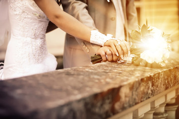 A newly wedding couple place their hands on a wedding bouquet showing off their wedding rings.