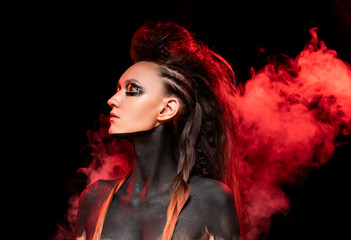 Portrait of a young savage girl in red smoke. Naked shoulders and neck are covered with black...