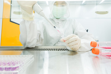 A scientist in sterile coverall gown preparing growth medium and reagent for cell cuture assay in...