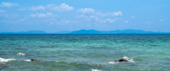 Landscape wide shot elective focus of the sun glimmering sunlight peaking the waving sea surface in hot summer sunny day with blue sky, white clouds and mountains backgrounds