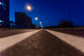 an asphalt road leading to the city at night from the outskirts. photo from the middle of the road at night with lanterns lighting