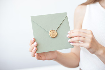 Close-up photo of female hands holding a silver blue or pink invitation envelope with a wax seal, a...