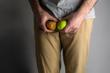 A man in beige jeans at the level of the genitals , holding a ripe and rotten apple. Disease for...