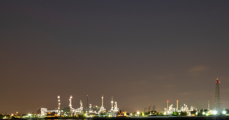 Long exposure night photo crude oil refinery plant and many chimney with petrochemical tanker or cargo ship at coast of the river with colorful bright light from lamp at thailand
