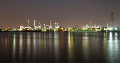 Fototapeta na wymiar Long exposure night photo crude oil refinery plant and many chimney with petrochemical tanker or cargo ship at coast of the river with colorful bright light from lamp reflect on water at thailand
