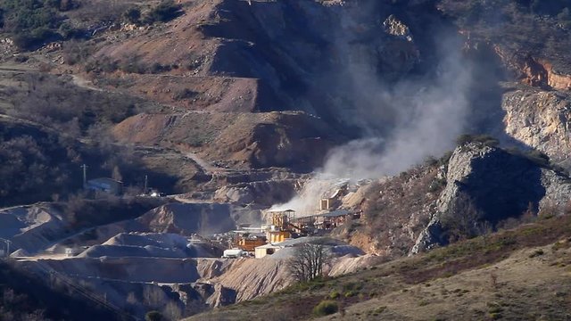 Cantera en la base de una monta&ntilde;a con maquinaria en  actividad y soltando polvo . Toma con teleobjetivo