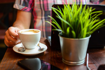 Cropped shot of a man's hands typing on a laptop that is on a wooden desk with a mug of coffee alongside.