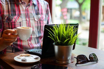 Business and technology concept. Pensive casual business man, freelancer, programmer using cofee while working on laptop computer thinking about his project in modern office, close up.