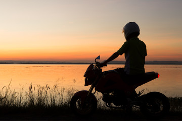 Fototapeta na wymiar Young biker over sunset, male riding motorcycle, motorbike driver traveling, girl racing on the lake road, freedom lifestyle.Ubolrat dam,khonkaen,thailand.
