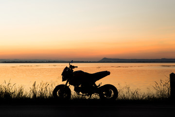 Motorcycle  in silhouette at sunset at lake.