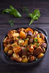 Fried beef and  potatoes with onions and garlic served in black dish on wooden background