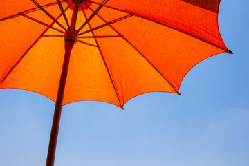 Fototapeta na wymiar Orange color beach umbrella made of wooden for protected sunlight with a bright blue sky background.