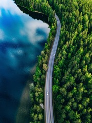Luftaufnahme der Straße zwischen grünem Wald und blauem See in Finnland