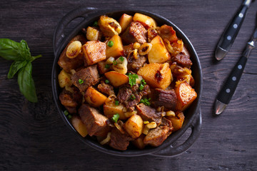 Fried beef and  potatoes with onions and garlic served in black dish on wooden background