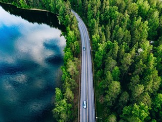 Aerial view of road between green forest and blue lake in Finland