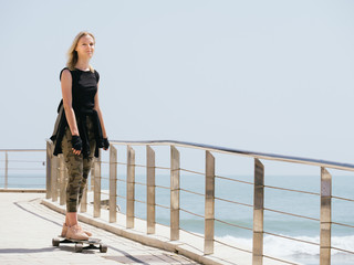 A beautiful blonde girl on skateboard in summer hot day on seafront