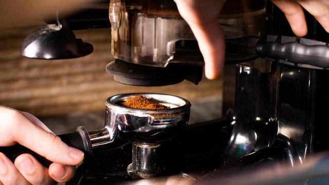 Barista man is grinding coffee using hand coffee grinder pushing handle, coffee pours into the holder, closeup hands.