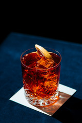 Negroni IBA cocktail, with gin, bitter, vermut, and orance slice. Colorful, and dark background.