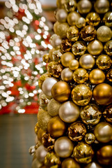 Gold holiday and Christmas ornament hanging from the tree surrounded by lights with a bokeh in the background.