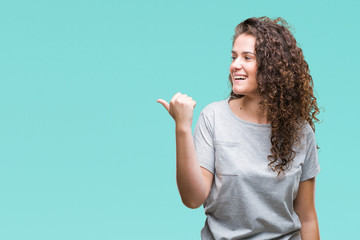 Beautiful young brunette curly hair girl wearing casual look over isolated background smiling with happy face looking and pointing to the side with thumb up.