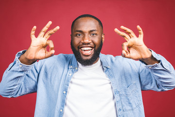 Happy young African-American man isolated against red background. Ok sign.
