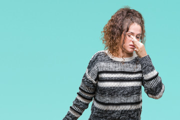 Beautiful brunette curly hair young girl wearing glasses over isolated background smelling something stinky and disgusting, intolerable smell, holding breath with fingers on nose. Bad smells concept.