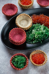 Red caviar and chuka salad with vegetable tartlets, close-up, vertical shot