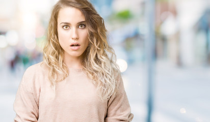 Beautiful young blonde woman wearing sweatershirt over isolated background afraid and shocked with...
