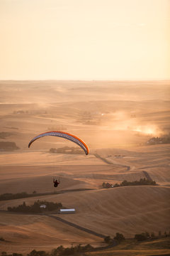 A man flies off into the sunset above dust filled rolling farm lands like a sky cowboy while on a father and son paragliding outing near Moscow, Idaho.