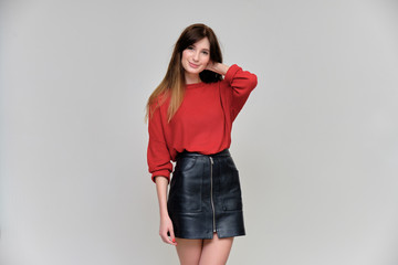 Photo portrait of a beautiful pretty brunette girl in a red sweater on a gray background. A woman is satisfied with her life, she stands in front of the camera, smiling and talking. Made in a studio.