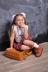 Portrait of beautiful smiling young first-grader with red suitcase on blackboard background. school and education concept