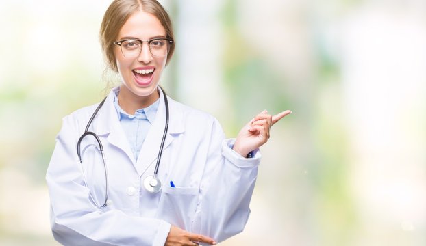 Beautiful young blonde doctor woman wearing medical uniform over isolated background with a big smile on face, pointing with hand and finger to the side looking at the camera.