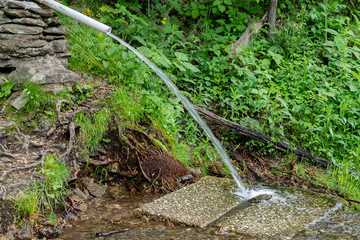 Color photo of clean spring water flowing from a mountain stream in the mountains of North Carolina. A PVC pipe is used to pipe the water out.