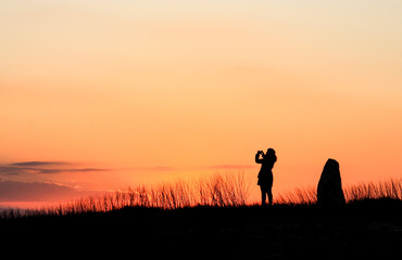 Silhouette of woman taking picture over sunset sky background