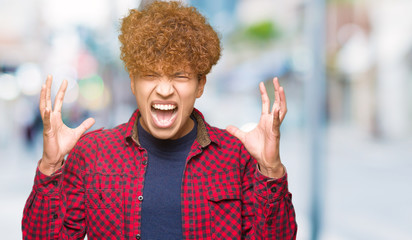 Young handsome student man with afro hair wearing a jacket celebrating mad and crazy for success with arms raised and closed eyes screaming excited. Winner concept