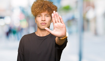 Young handsome man with afro hair wearing black t-shirt doing stop sing with palm of the hand. Warning expression with negative and serious gesture on the face.