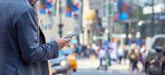 New York, Wall street. Young man in suit holding a smartphone
