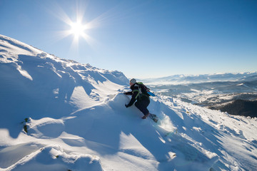 Tourist hiker climber in winter clothing with backpack climbing dangerous rocky steep mountain slope covered with deep snow, white sun rays shining in bright blue sky copy space background.