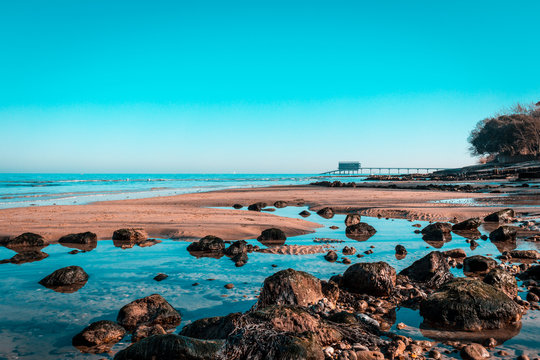 Bembridge Lifeboat Beach and reflective rock pools, bright blue teal sky