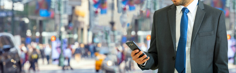 New York, Wall street. Young man in suit holding a smartphone