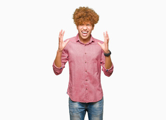 Young handsome business man with afro hair crazy and mad shouting and yelling with aggressive...