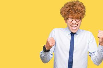 Young handsome business man with afro wearing glasses very happy and excited doing winner gesture with arms raised, smiling and screaming for success. Celebration concept.